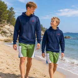 Två killar i olika åldrar bär blå, vita och gröna badshorts på stranden – kort surfmodell för barn.