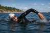Kvinna i svart våtdräkt för open water simning stående vid vatten